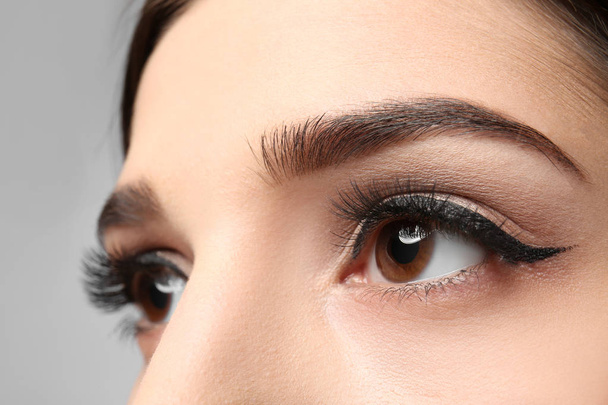 Young woman with elegant makeup and long eyelashes on grey background. Eyelash extensions - Fotografie, Obrázek