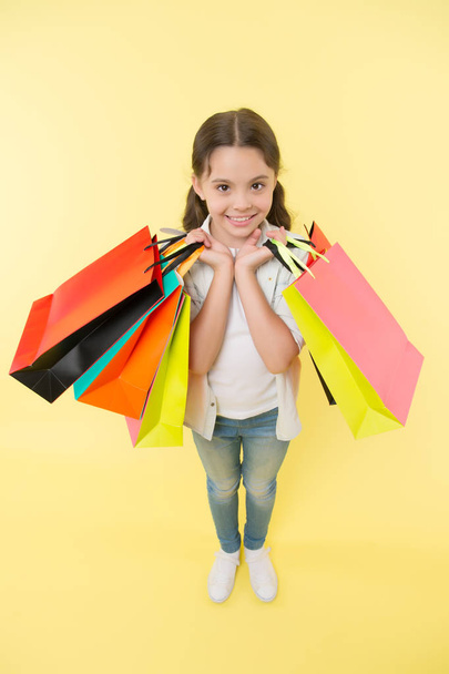 All for me. Kid girl happy smiling face carries bunch packages yellow background. Birthday girl concept. Girl likes to get gifts and birthday presents. Kid happy celebrating birthday with gifts. - Foto, Bild