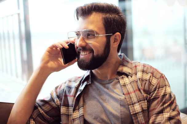Handsome trendy hipster talking on mobile phone in cafe - Zdjęcie, obraz