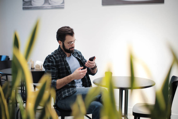 Handsome trendy hipster using mobile phone in cafe - Photo, Image