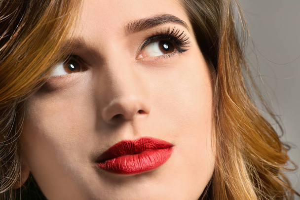 Young woman with elegant makeup and long eyelashes on grey background. Eyelash extensions - Fotó, kép