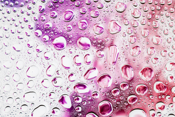 Close-up van een druppel water tegen een paars, roze en oranje rook op witte achtergrond, condensatie op de achtergrond van een gradiënt - Foto, afbeelding
