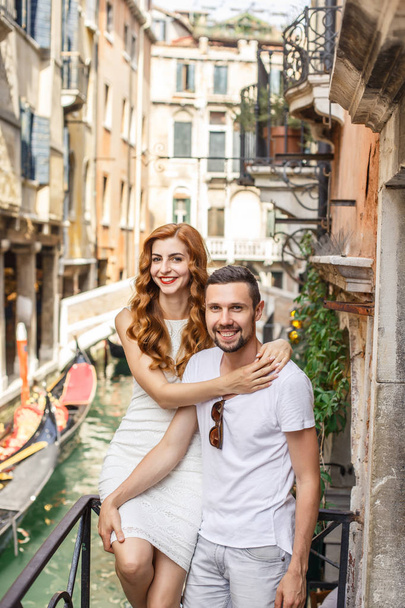 Young couple posing on balcony over the canal with bridge and gondola - Фото, изображение