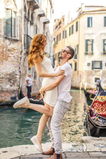 Young man raises his girlfriend up above the quay of canal in Venice - Фото, изображение