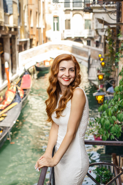 Attractive redhead woman posing on balcony over the canal with bridge and gondola - Foto, immagini