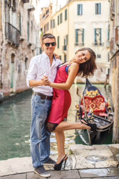 Young man embracing his girlfriend on quay of canal in Venice - 写真・画像