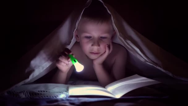 Dítě čte knihu pod deky s baterkou v noci. chlapec s světlé vlasy a modré oči - Záběry, video