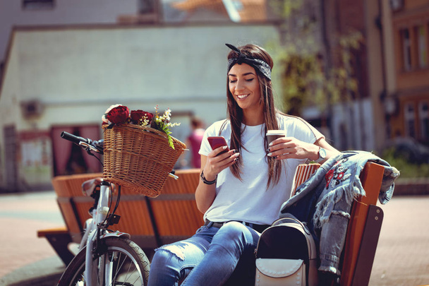 mladá žena s kolo s květinový koš pomocí smartphone a pití kávy - Fotografie, Obrázek