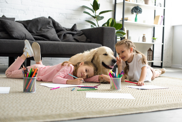 smiling kids lying on floor together with golden retriever dog at home - Photo, Image
