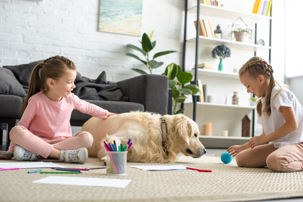 little children playing with golden retriever dog on floor at home - Foto, immagini