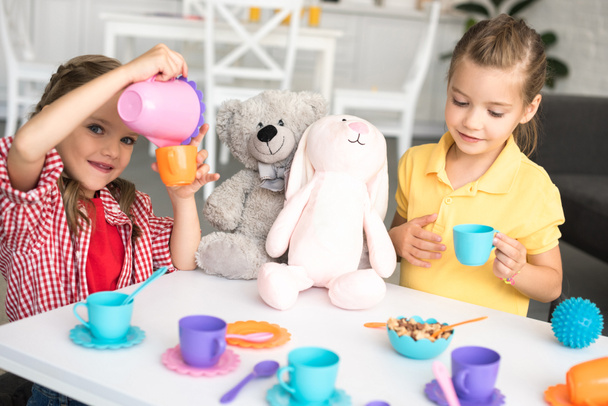 adorable little sisters pretending to have tea party together at home - Photo, Image