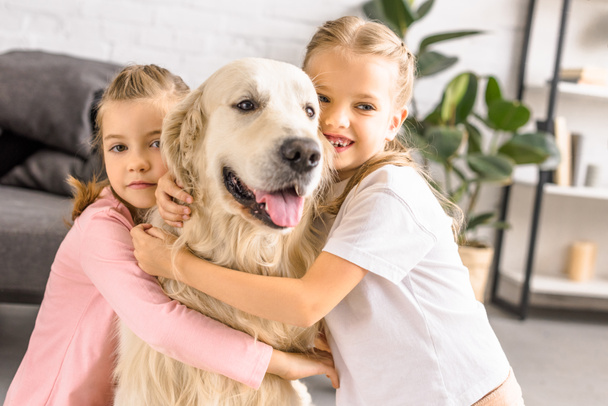 portrait of adorable smiling kids hugging golden retriever dog at home - Photo, Image