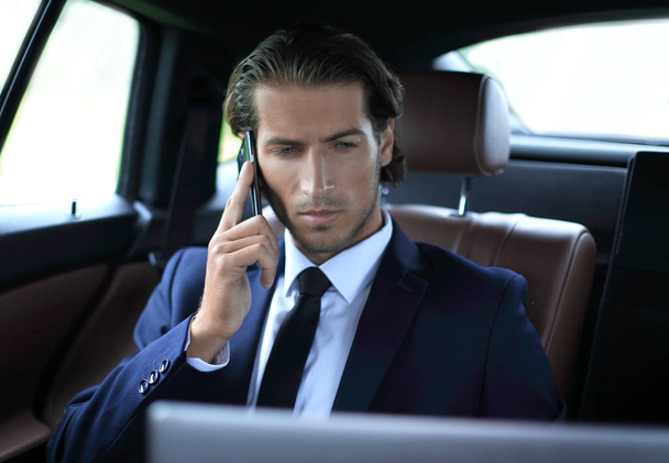 Handsome businessman using mobile phone in car. - Foto, afbeelding