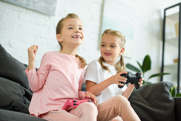 retrato de hermanas pequeñas con gamepads jugando videojuego juntas en casa
 - Foto, Imagen