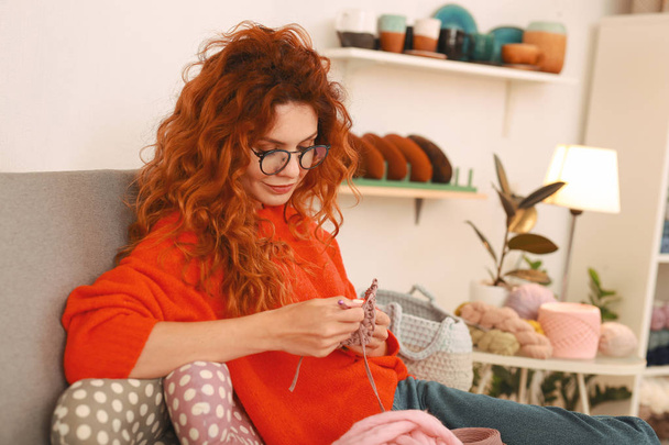 Girl with ginger hair wearing glasses knitting baby clothes - Фото, зображення