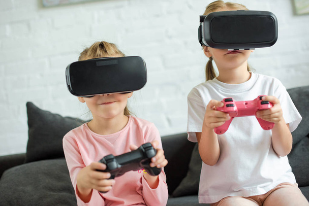 obscured view of kids in virtual reality headsets playing video game on sofa at home - Foto, imagen
