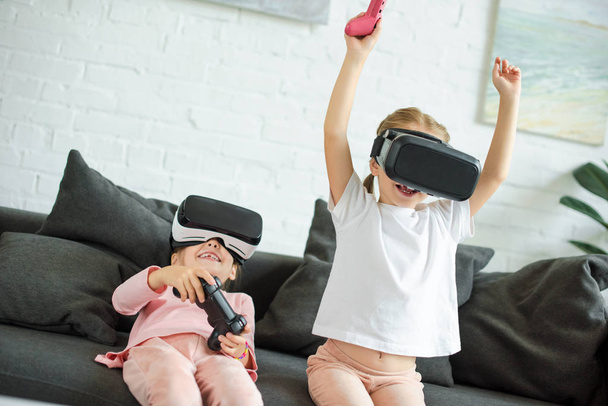 obscured view of kids in virtual reality headsets playing video game on sofa at home - Фото, изображение