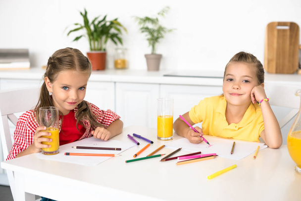 ritratto di simpatici bambini sorridenti che guardano la macchina fotografica mentre disegnano immagini a tavola a casa
 - Foto, immagini
