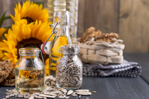 Sunflower oil and large yellow flowers. Oil in the bottle. A wooden background, seeds and a biscuit with nuts and seeds. Organic food. Copy space - Zdjęcie, obraz