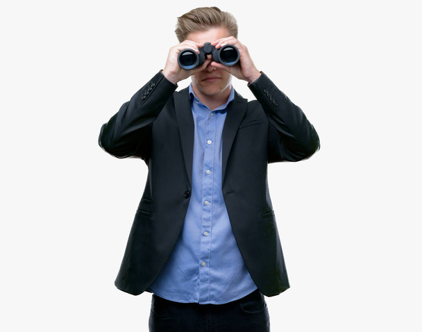 Young handsome blond man looking through binoculars with a confident expression on smart face thinking serious - Photo, Image