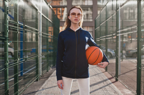 Sports girl confident in a Sunny evening standing at the basketball court with a basketball at hand - Фото, зображення