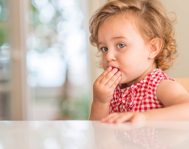 Gyönyörű szőke gyermek kék szemekkel eszik eper otthon. - Fotó, kép