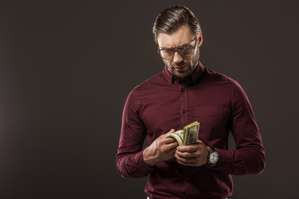 serious man in eyeglasses counting dollar banknotes isolated on black - Foto, Imagen