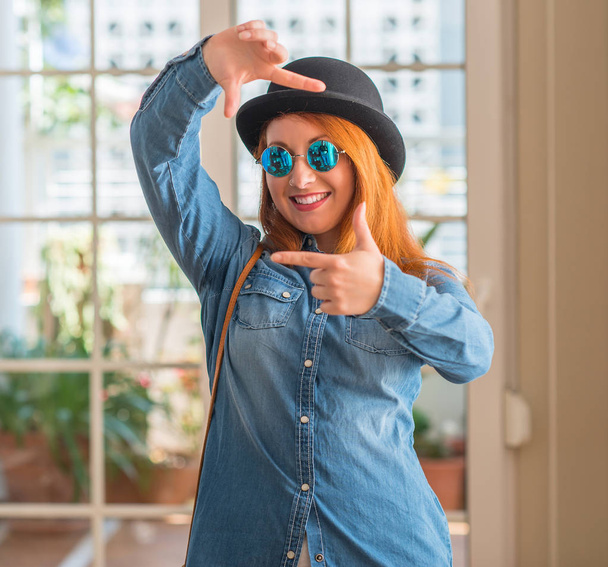 Stylish redhead woman wearing bowler hat and sunglasses smiling making frame with hands and fingers with happy face. Creativity and photography concept. - Zdjęcie, obraz