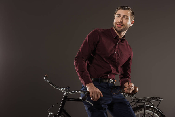 handsome smiling young man sitting on bicycle and looking away on black - Foto, Imagen