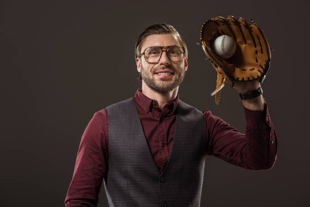 handsome smiling buisnesssman in eyeglasses holding ball with baseball glove isolated on black - Foto, imagen