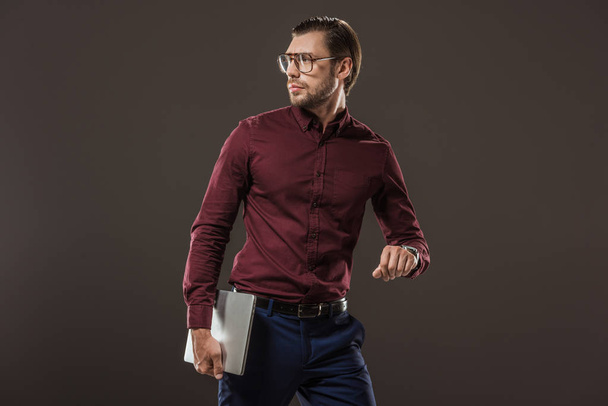 man in eyeglasses holding laptop and looking away isolated on black - Photo, Image