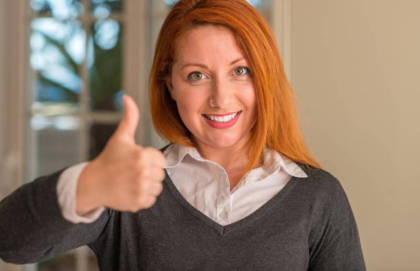 Kızıl saçlı kadın, kocaman bir gülümseme ile ok işareti yapıyor mutlu ev, parmaklarıyla, mükemmel işaret parmak - Fotoğraf, Görsel