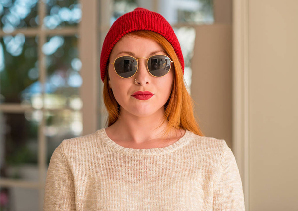 Elegante donna rossa che indossa berretto di lana e occhiali da sole con un'espressione fiduciosa sul viso intelligente pensando serio
 - Foto, immagini