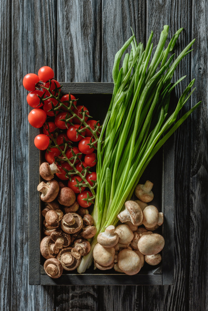 top view of champignon mushrooms with leeks and cherry tomatoes in box on wooden tabletop - Foto, afbeelding