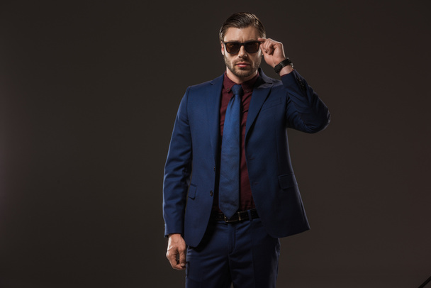 schöner stylischer Geschäftsmann mit Sonnenbrille auf schwarzem Hintergrund  - Foto, Bild