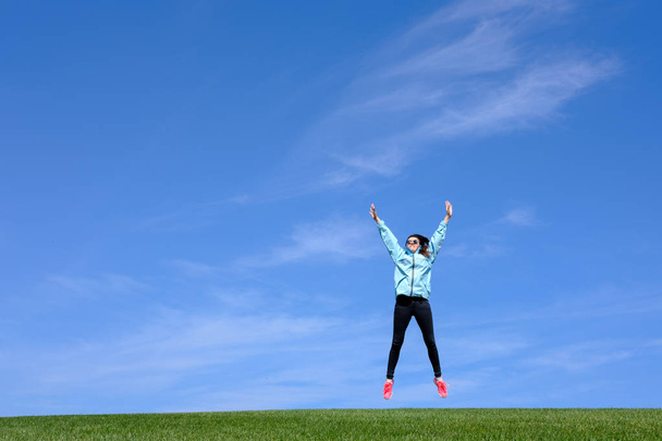 pretty young woman jumping on green grass lawn over blue sky - Φωτογραφία, εικόνα