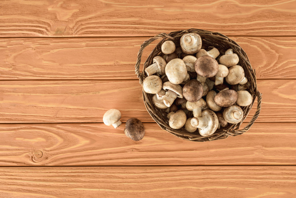 top view of raw champignon mushrooms in basket on wooden surface - Fotó, kép
