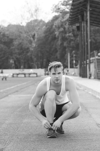 Concept of marathon and competition. Sportsman ties his trainers sitting and getting ready to run - 写真・画像