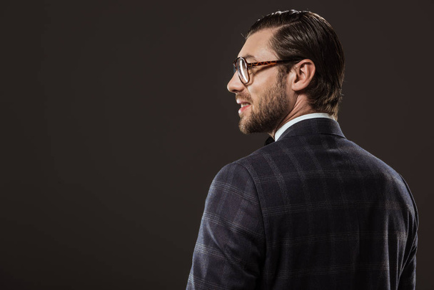 back view of handsome smiling man in eyeglasses looking away isolated on black - Foto, Imagem