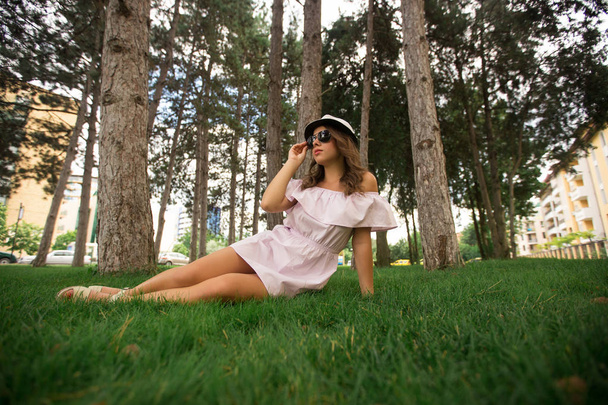Kaunis tyttö indress ja hattu puistossa. Vihreää ruohoa ja aurinkoista. Puiden taustaa
 - Valokuva, kuva