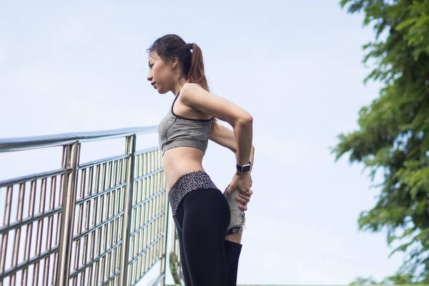 Fitness sport κορίτσι αθλητικά μόδας κάνει γιόγκα άσκηση γυμναστήριο στην οδό. FIT νεαρός ασιατική γυναίκα κάνει προπόνηση πρωί. Νέοι ευτυχισμένη γυναίκα της Ασίας που εκτείνεται στο πάρκο μετά την εκτέλεση προπόνηση. - Φωτογραφία, εικόνα