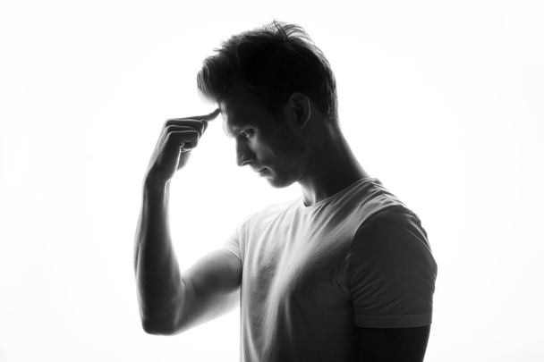 young thoughtful man standing on white background touching his forehead with finger, side view - Foto, Imagen
