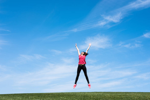 pretty young woman jumping on green grass lawn over blue sky - Фото, изображение