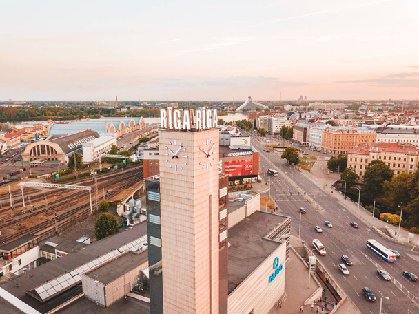 RIGA, LATVIA - JUNE 14, 20: Aerial view on the main station and shopping mall Origo clock tower during sunset. The tower rises over city with Riga naming on top of it. - Foto, Bild