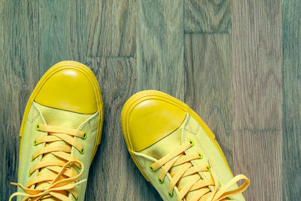 одна пара желтой модной обуви в спортивном стиле крупным планом на абстрактном фоне пустого паркетного пола
 - Фото, изображение