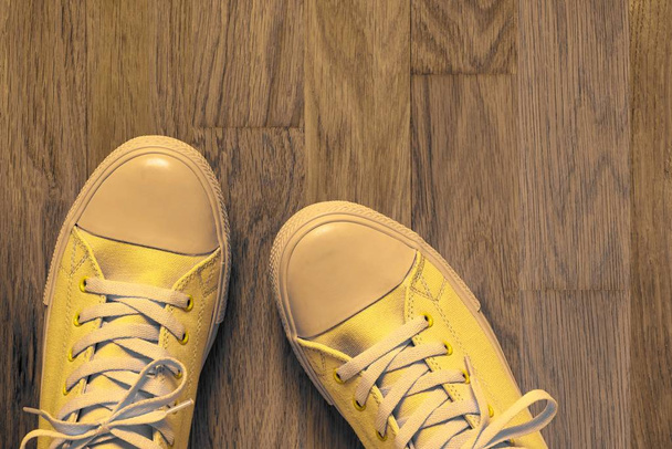 ein Paar gelber modischer Schuhe in Nahaufnahme im Sportstil auf einem abstrakten Hintergrund eines leeren Parkettbodens - Foto, Bild