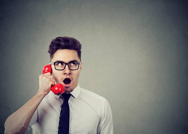 Amazed shocked young business man talking on a red telephone  - Photo, Image