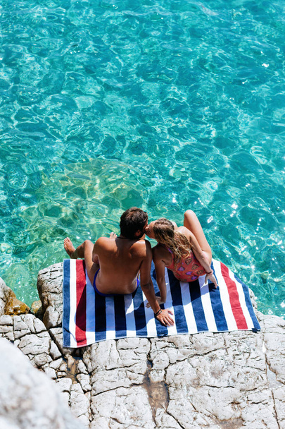 Boyfriend and girlfriend sitting on rock by the sea and kissing. - Zdjęcie, obraz