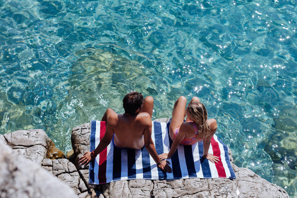 Boyfriend and girlfriend sitting on rock by the sea and sunbathing. - Zdjęcie, obraz