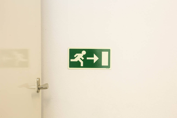 La señal de salida de emergencia muestra la dirección de escape en caso de peligro. El tablero de salida de emergencia cuelga en el techo del edificio
. - Foto, Imagen